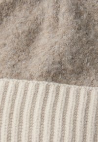 Tessuto beige peloso con una texture morbida nella parte superiore, che si trasforma in un motivo a coste color crema alla base.