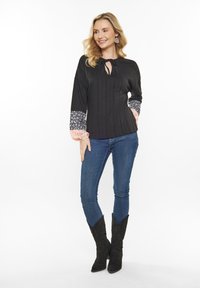 Top nero con texture e scollatura a chiave, maniche a palloncino stampate in blu navy e pesca, abbinato a jeans skinny blu e stivali neri in camoscio.