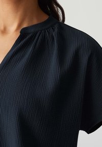 Haut bleu marine foncé présentant un tissu texturé froissé, un col plissé et des manches courtes avec une coupe décontractée et un design simple.