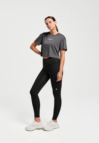 Grijze, korte sport T-shirt met korte mouwen, gecombineerd met zwarte leggings en witte sneakers; bevat logodetails op beide kledingstukken.