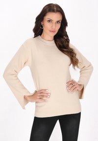 Pulover bej din lână, cu un model texturat, decolteu rotund și mâneci în clopot. Asortat cu pantaloni negri, prezentând o croială lejeră.