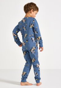 Sininen puuvillapijama-setti, jossa on kuviointina kilpa-autoja ja ruudullisia lippuja. Pitkät hihat ja housut, joissa on ribbireunat. Pehmeä tekstuuri.
