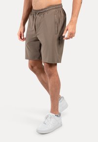 Braune Sportshorts mit elastischem Bund, Kordelzug, Seitentaschen und glatter Textur, kombiniert mit weißen Sneakern.