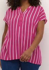 Haut rayé rose et blanc avec un col à encoche boutonné, des manches courtes et une coupe décontractée. Le tissu semble léger avec une texture lisse.