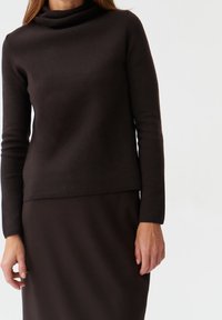 Maglia marrone lavorata a maglia con collo a scialle, maniche lunghe e design aderente, abbinata a una gonna marrone coordinata, tessuto liscio e senza motivi visibili.