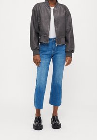 Šedá umělá kožená bomber bunda s vroubkovanými manžetami a lemem, v kombinaci s světle modrými zkrácenými džíny a černými platformovými mokasínami se cvočky.