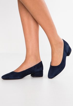 Granatowe zamszowe buty na niskim obcasie z ostrym noskiem i subtelnymi wycięciami po bokach. Teksturowane wykończenie oraz solidny, blokowy obcas.