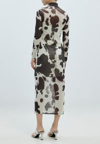 Langärmliges Kleid aus leichtem Stoff mit einem cremefarbenen Grund und unregelmäßigen braunen und schwarzen Flecken. Knielang mit einer figurnahen Silhouette.
