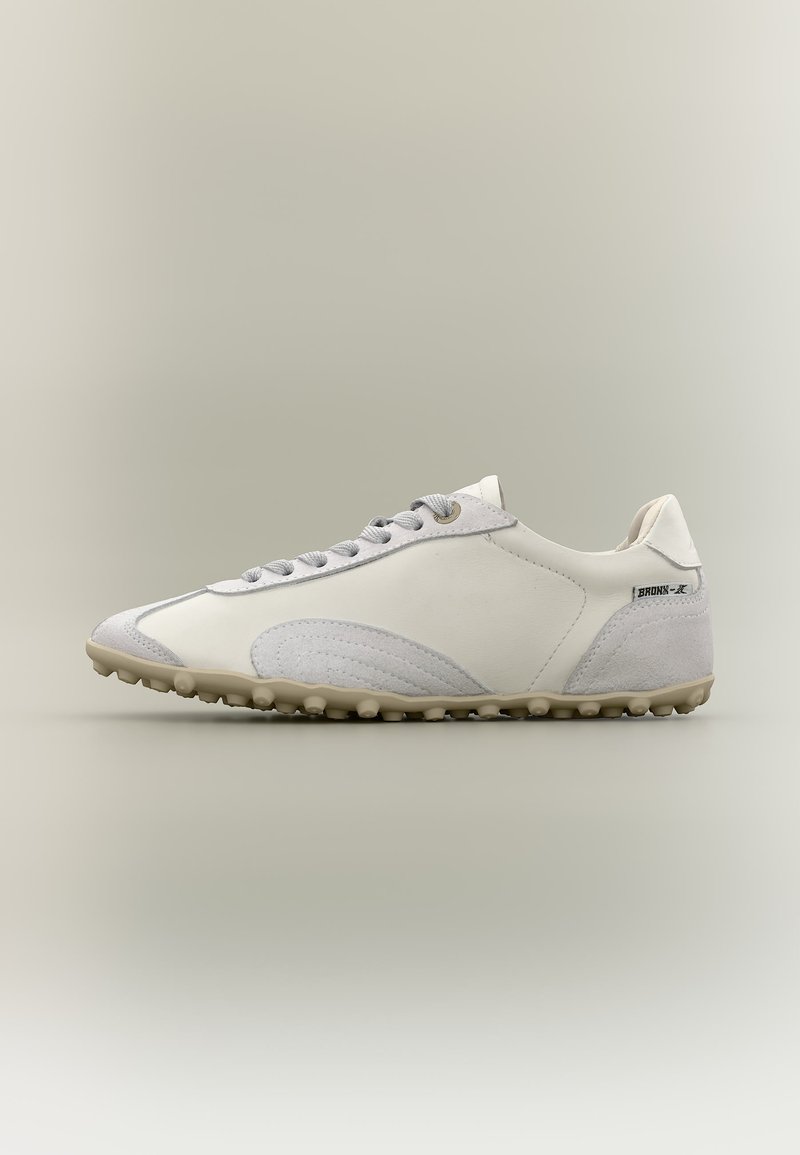 Λευκό και γκρι ανοιχτόχρωμο sneaker χαμηλού προφίλ με υφή σόλας, κορδόνια στο μπροστινό μέρος και ετικέτα «BRONX» κοντά στη φτέρνα σε ουδέτερο φόντο.