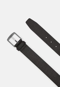 Ceinture en cuir noir avec une surface texturée, boucle en métal argenté et plusieurs trous pour le réglage de la taille. Présente un design minimaliste.