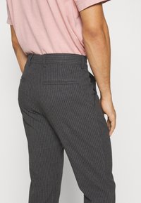 Tmavě šedé proužkované kalhoty slim fit, s páskem a dvěma kapsami, v kombinaci se světle růžovou košilí. Texturovaná látka.