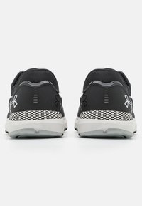 Zwarte sportschoenen met een gestructureerd mesh bovenwerk, een kenmerkend logo, een cushioned zool en witte gemusterde accenten op de hiel en buitenzool.