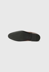 Semelle en cuir avec une tige lisse en marron et une semelle extérieure en caoutchouc noir dotée d'un motif en vagues pour une meilleure traction et durabilité.