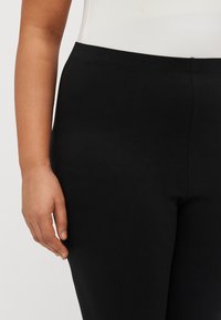 Zwarte leggings van rekbare, гладкое stof. Voorzien van een brede tailleband en een slanke pasvorm, zonder zichtbare patronen of hardware.