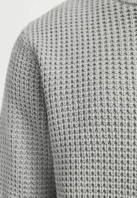 Suéter gris de punto con un patrón texturizado en forma de waffle, corte holgado y cuello redondo. Tejido suave visible en detalle de cerca.