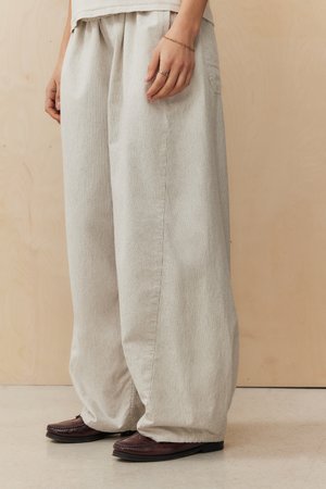 Pantalons larges gris clair en tissu texturé avec des rayures verticales, offrant une coupe décontractée et une taille élastiquée avec cordon de serrage. Assortis avec des chaussures foncées.