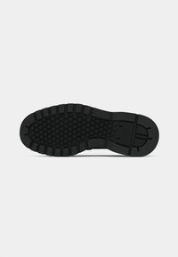 Semelle de chaussure en caoutchouc noir avec un motif hexagonal texturé, de profonds rainures et des bords striés pour la traction. Design global plat et robuste.