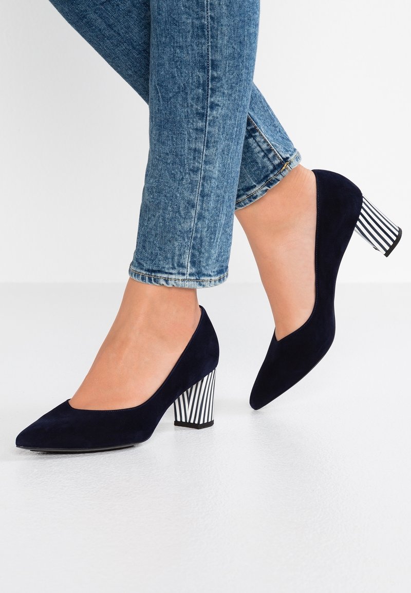 Femme portant des escarpins en daim bleu foncé avec des talons épais rayés noir et blanc et un jean skinny bleu.