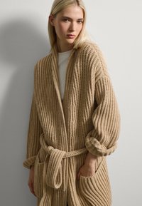 Beige geribd gebreide cardigan met een sjaalkraag, lange mouwen, een strikceintuur en voorzakken. Getextureerde stof met een gezellige uitstraling.