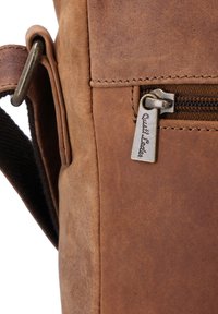 Szczegół brązowej skórzanej torby z zamkiem błyskawicznym i metalowym uchwytem, ukazujący gładką teksturę i subtelne przeszycia wzdłuż krawędzi.