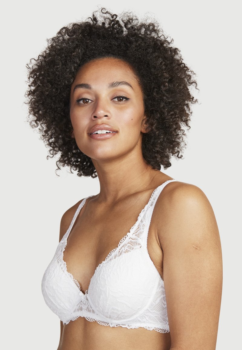 Witte kanten bralette met bloemenpatroon, zachte cups, verstelbare banden en een golfrand. Ontworpen voor comfort en ondersteuning.