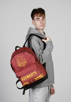 Rode Gryffindor-thema rugzak met gouden accenten en tekst. Kenmerkt een gladde stofoppervlakte, twee schouderbanden en een zwarte onderkant.