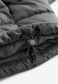 Tissu matelassé noir avec un cordon de serrage et un bouchon en plastique utilisés pour ajuster l'ajustement sur le bord d'un vêtement ou d'un sac.
