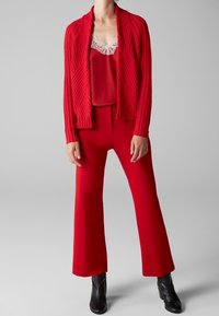 Un cardigan rouge à côtes sur un débardeur rouge avec des bordures en dentelle, associé à un pantalon évasé rouge taille haute et des bottines noires.