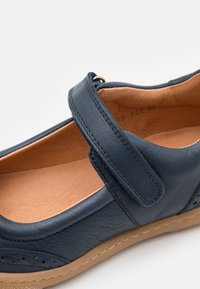 Granatowe skórzane buty z rzepem, o zaokrąglonym kształcie i jasnobrązowym wnętrzu, z perforowanymi detalami po zewnętrznej stronie.