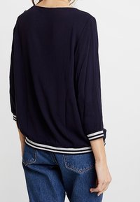 Blusa leggera color navy con maniche a tre quarti, polsini a righe, scollatura rotonda e un design con vestibilità comoda. Abbinata a jeans in denim.