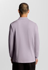 Polo a maniche lunghe in lavanda chiaro. Realizzato in un tessuto morbido, con colletto piatto e spacchi laterali all'orlo. Design semplice e privo di decorazioni.