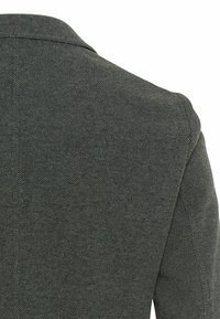 Gros plan de la zone de l'épaule arrière d'un blazer texturé gris foncé montrant le motif du tissu et les détails des coutures.