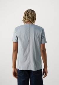 Tricou scurt, cu mânecă scurtă, de culoare gri deschis, cu croială dreaptă, având o cusătură la spate și o textură netedă și moale. Asortat cu blugi din denim închis.