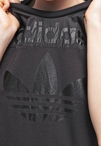 Top deportivo negro con un logo brillante de adidas y diseño de trébol. Confeccionado con una tela suave, cuenta con un escote circular y mangas cortas.