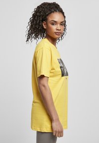 Gul bomull T-shirt med avslappnad passform, korta ärmar och svart grafiskt tryck på framsidan, slät textur och standard rund hals.