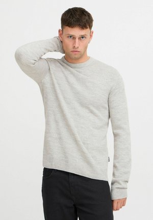 Suéter de punto gris claro con cuello redondo y puños acanalados, que presenta un patrón texturizado. Combinado con jeans de denim oscuro.