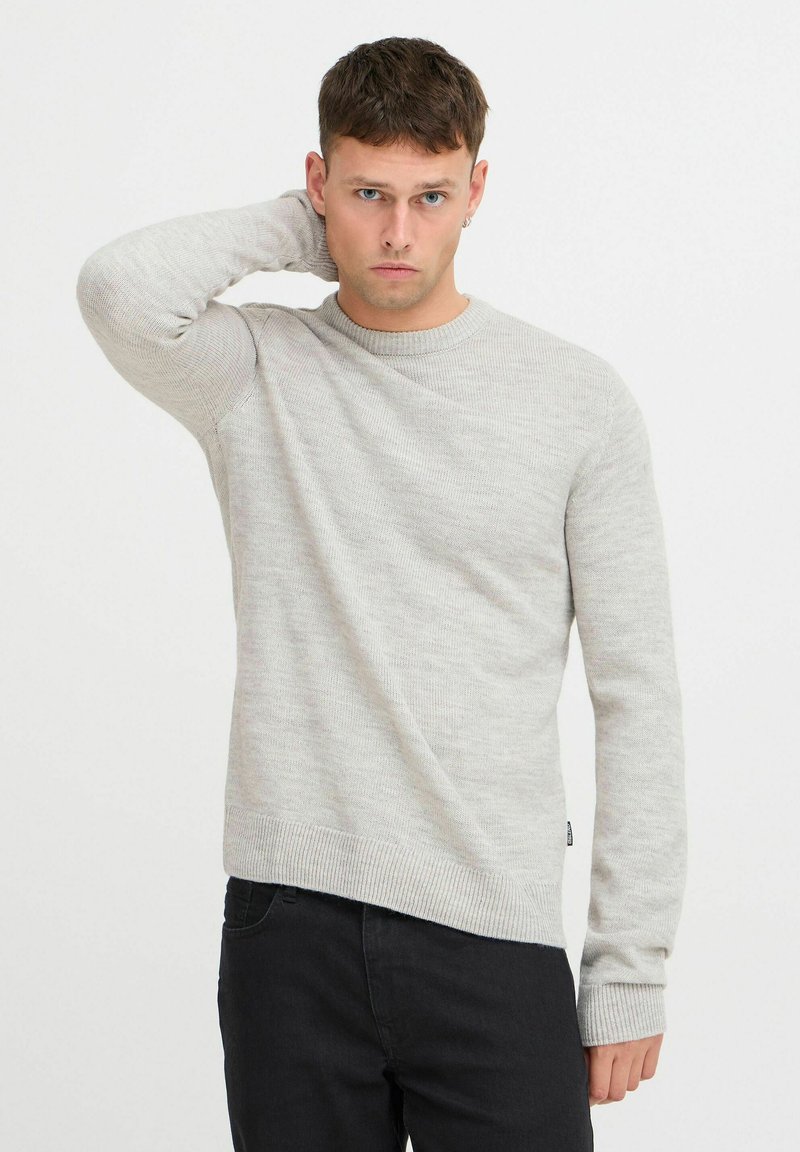 Maglione grigio chiaro a maglia con colletto rotondo e polsini a costine, caratterizzato da un motivo testurizzato. Abbinato a jeans in denim scuri.