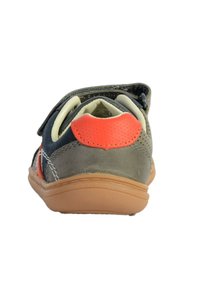 Scarpa in suede grigia con dettagli arancioni e suola in gomma. Presenta una fibbia in velcro e una forma arrotondata. L'interno è rivestito di colore crema.