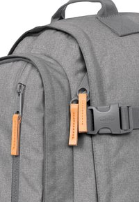 Zaino in tessuto grigio caratterizzato da un design senza cuciture, zip prominente e dettagli in pelle sulla linguetta della zip. Include una fibbia in plastica.