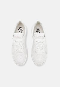 Baskets en cuir blanc avec une boîte à orteils perforée, des lacets plats et un col rembourré. Présente une marque sur la languette et à l'intérieur. Texture lisse.