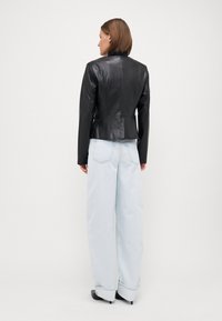 Black leather jacket with a fitted waist, smooth texture, and tailored design, paired with light blue wide-leg jeans.