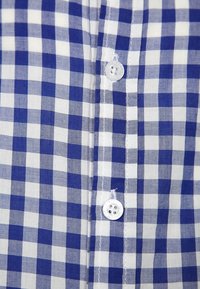Niebiesko-biała koszula w kratę z przodem na guziki, o gładkiej fakturze, z plastikowymi guzikami i wyraźnym wzorem w kratę.