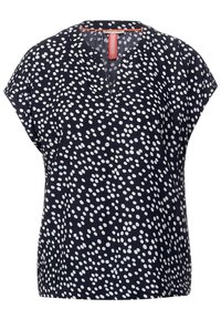 Navyblå blus med vita spridda prickar, korta ärmar och en inskärning vid halsen med en korallfärgad detalj på insidan av kragen.