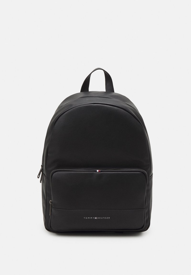 Mochila negra de Tommy Hilfiger con bolsillo frontal con cremallera y asa superior, mostrada sobre un fondo blanco.