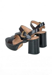 Sandalias de plataforma de cuero negro con un tacón grueso, que presentan un diseño de tiras cruzadas y un acento de hardware circular dorado.