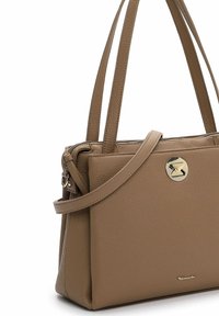 Tan lædertaske med dobbelt håndtag, en aftagelig rem, hardware i guldtoner og lynlås lukning. Har struktureret materiale og logo detaljer.