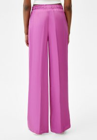 Wijduitlopende broek in een levendige roze satijnen stof met een elastische tailleband, een gladde textuur en geen zichtbare zakken of versieringen.