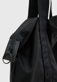 Black nylon bag featuring a zip closure, thick fabric handles, and a rectangular shape, with a textured logo on the strap.