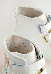 Weiße High-Top-Schuhe mit Innenfutter im pastellfarbenen Sternenmuster, ausgestattet mit bunten Klettverschlüssen und dekorativen Stern- und Regenbogenakzenten.