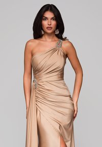 Vestido beige de un solo hombro hecho de una tela suave con detalles fruncidos, acentos de joyas en el hombro y la cintura, con una abertura alta en el muslo.